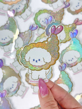 Load image into Gallery viewer, Glittery dog-shaped sticker held by a hand with pink nail polish on a sheet of similar stickers.