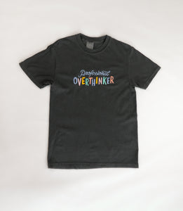 A graphite grey, 100% cotton t-shirt with a playful, embroidered message that reads "Professional Overthinker" in colorful, handwritten-style lettering. The shirt has a relaxed, unisex fit, perfect for everyday wear.