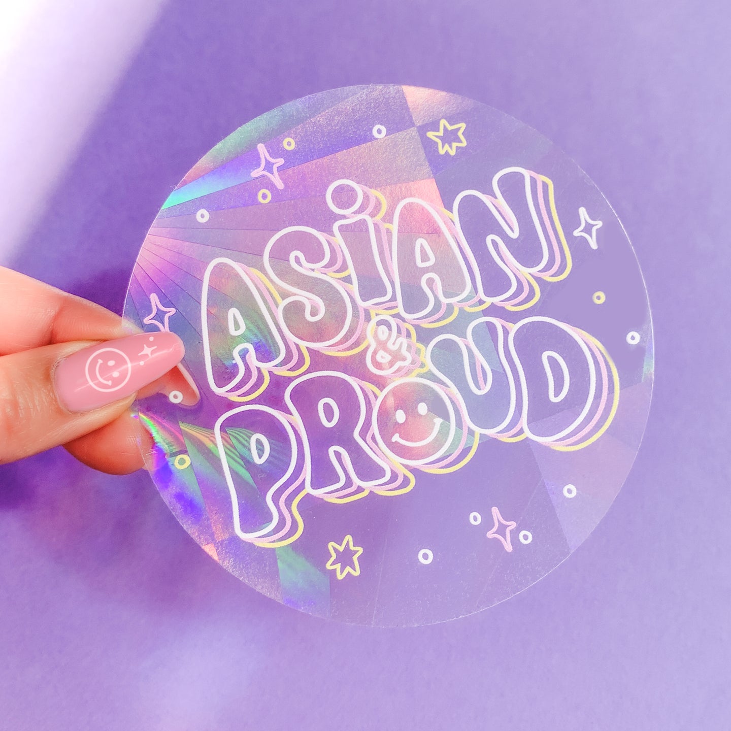 A circular, holographic sticker that changes colors in direct sunlight, displaying vibrant rainbow hues. The sticker features the phrase 