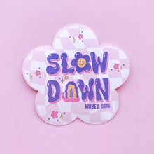 Load image into Gallery viewer,  A vinyl sticker in the shape of a flower, featuring the phrase &quot;SLOW DOWN&quot; in bold, colorful letters. A cheerful smiley face and other playful elements decorate the sticker, adding a touch of positivity. It&#39;s a reminder to take things at your own pace and enjoy the journey. The sticker measures 3.5 inches by 3.4 inches and is perfect for adding a touch of personality to your belongings.
